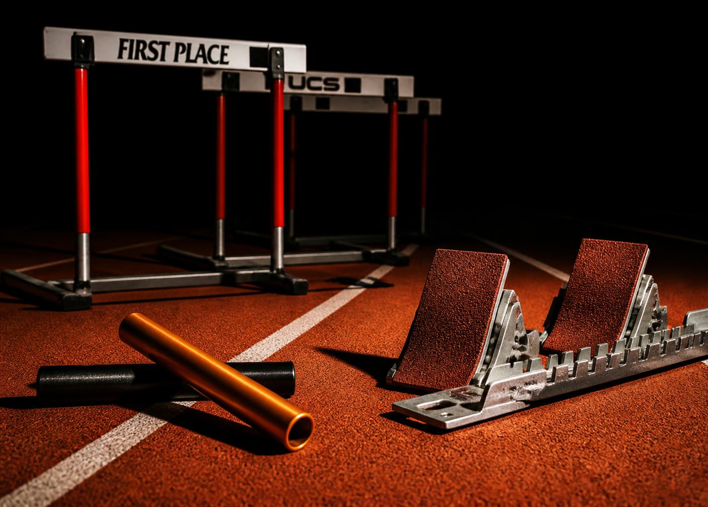 Hurdles, starting blocks and a relay baton on a track under dramatic lighting
